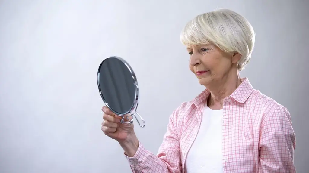 Photo of older woman looking at mirror with regret.