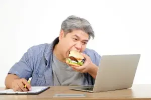 Photo of overweight man eating a burger at his desk.