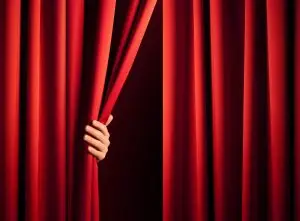 Photo of someone pulling a theater curtain open to start the second act.