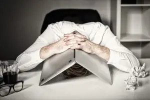 A photo of a burned-out man hiding under his laptop.