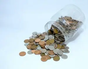 Photo of a jar tipped over and spilling coins of all denominations.