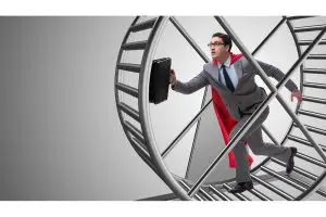 Photo of businessman wearing a Superman cape and running on a hamster wheel.